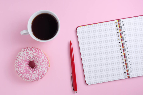 Directly above view of pink donut with coffee and notebook on colored background - Foto, immagini