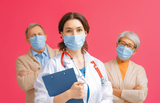 Doctor and senior couple wearing facemasks during coronavirus and flu outbreak. Virus protection, home quarantine. COVID-2019. Taking on masks. People on red pink color background. - Foto, Imagen