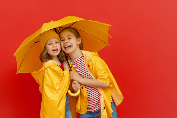 Happy emotional children laughing and embracing. Kids with yellow umbrella on colored red background. - Φωτογραφία, εικόνα