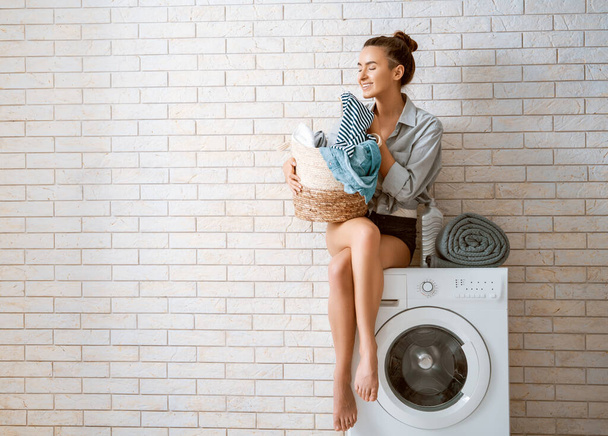 Beautiful young woman is smiling while doing laundry at home.  - Photo, image