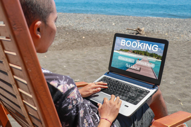 Concept de réservation de voyage, visites, hôtels et billets réservation en ligne. Jeune homme travaillant sur un ordinateur portable sur la plage avec du sable volcanique noir - Photo, image