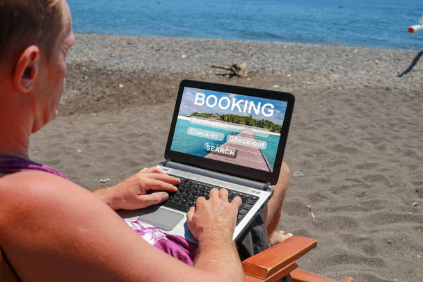 Concepto de reserva de viajes, tours, hoteles y entradas reserva en línea. Hombre joven trabajando en el ordenador portátil en la playa con arena volcánica negro - Foto, imagen