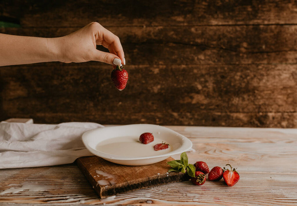 rozrzucone soczyste, świeże, czerwone truskawki na stole z klasyczną deską. Liść mięty. krople i plamy rozlanego mleka. deska do krojenia warzyw. Wysokiej jakości zdjęcie - Zdjęcie, obraz