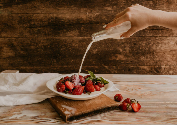 scattered juicy fresh red strawberries on the table with vintage plank. mint leaf. drops and splashes of spilled milk. vegetable cutting board. High quality photo - Photo, Image