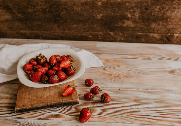 scattered juicy fresh red strawberries on the table with vintage plank. mint leaf. drops and splashes of spilled milk. vegetable cutting board. High quality photo - Foto, imagen