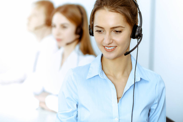 Call center operators. Focus on beautiful business woman in headset. - Фото, изображение