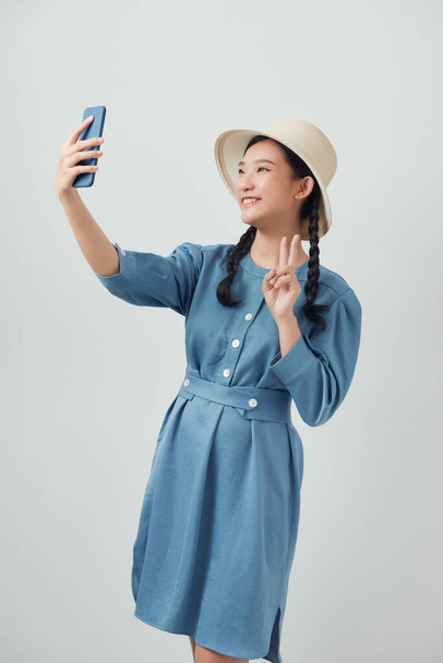Αστεία κοπέλα σε casual στυλ, pigtail μαλλιά, κρατώντας το κινητό έξυπνο τηλέφωνο και να κάνει selfie με ειρήνη ή νίκη σημάδι - Φωτογραφία, εικόνα