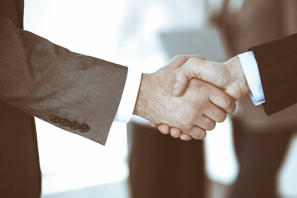 Business people shaking hands while standing with colleagues after meeting or negotiation, close-up. Group of unknown businessmen and women in modern office. Teamwork, partnership and handshake concept, toned picture. - Foto, Bild