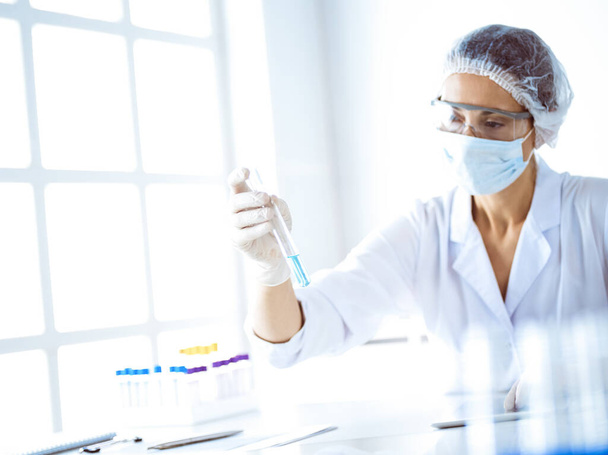 Professional female scientist in protective eyeglasses researching tube with reagents in laboratory. Concepts of medicine and science researching. - Foto, imagen
