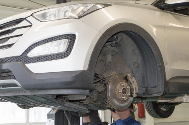 Egy autószerelő egy autószerelő műhelyben diagnosztizálja a felvonón függő könnyű autót. - Fotó, kép
