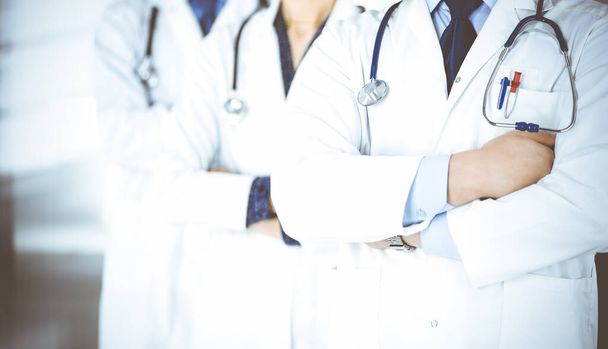 Group of modern doctors standing as a team with crossed arms and stethoscopes in hospital office. Physicians ready to examine and help patients. Medical help, insurance in health care, best desease treatment and medicine concept. - Photo, image