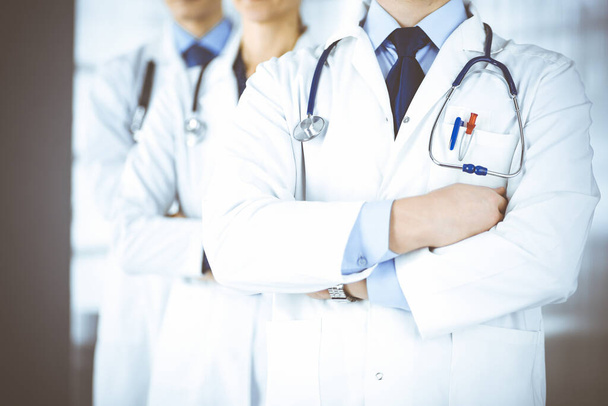 Group of modern doctors standing as a team with crossed arms and stethoscopes in hospital office. Physicians ready to examine and help patients. Medical help, insurance in health care, best desease treatment and medicine concept. - Photo, image