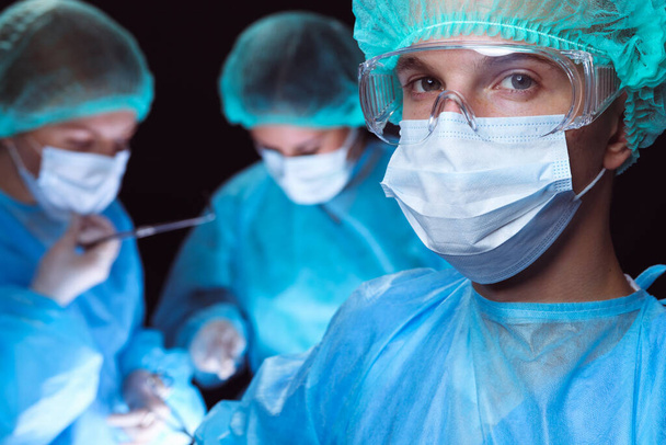 Group of surgeons wearing safety masks performing operation. Medicine concept - 写真・画像