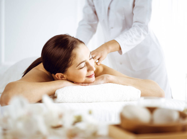 Beautiful brunette woman enjoying back massage with closed eyes. Spa and medicine concept - Фото, зображення