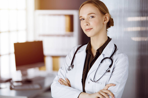 Cheerful smiling female doctor standing with arms crossed in clinic. Portrait of friendly physician woman. Medicine concept - Foto, Imagen