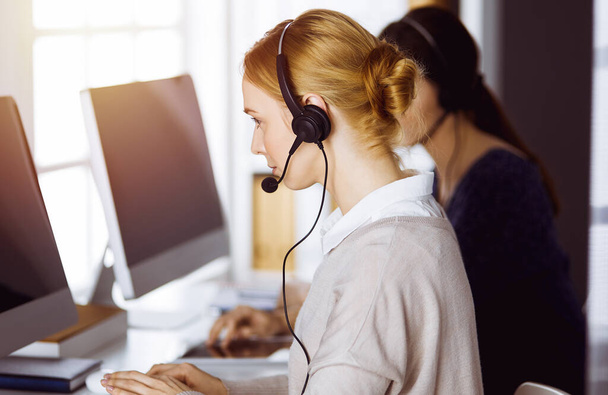Businesswoman talking by headset in sunny office. Call center and diverse people group in business. - Fotoğraf, Görsel