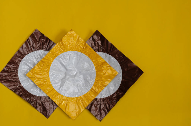 Three square pieces of colored foil on yellow. Pieces of foil brown and yellow with a white circle. Abstract background. Flat lay. - Photo, Image