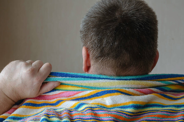 La parte posterior de un hombre maduro con una toalla de baño de color arco iris alrededor de sus hombros. Vista trasera de un hombre caucásico de mediana edad con el pelo canoso. - Foto, Imagen