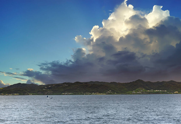 Маленькая японская рыбацкая лодка, плывущая по каналу Урага у Токийского залива с берегом полуострова Босо на заднем плане, с видом на огромное впечатляющее облако. - Фото, изображение