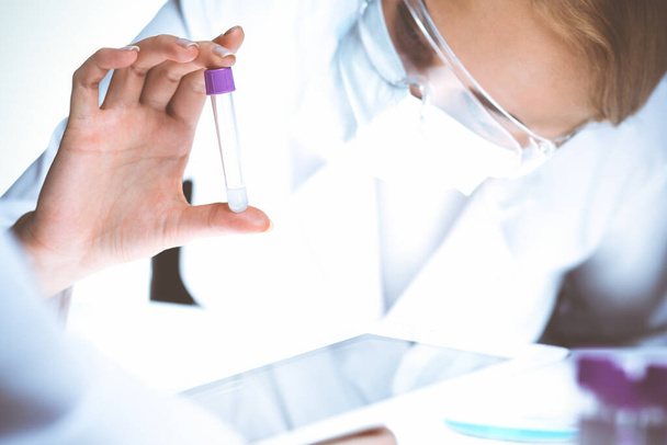Coronavirus pandemia. Ammattimainen naispuolinen tutkija suojalaseissa tutkimassa putkea reagensseilla laboratoriossa. Lääketieteen ja virussuojelun käsitteet. - Valokuva, kuva