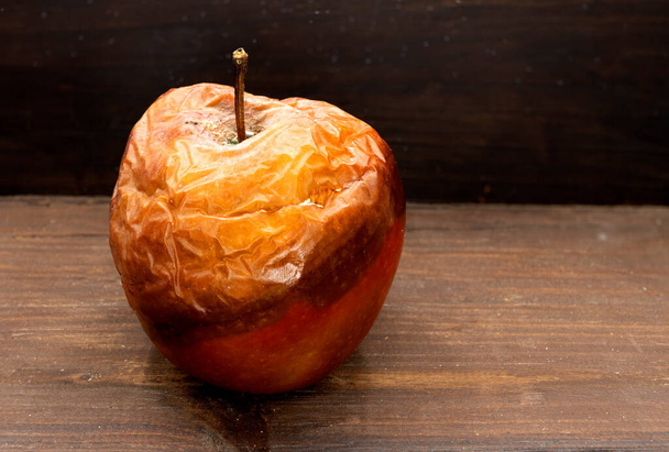 shnilé jablko, špatné jablko, plesnivé jablko, dřevěné pozadí - Fotografie, Obrázek