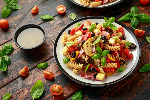 Antipastosalat mit Nudeln, Tomaten, Oliven, roten Zwiebeln, Paprika, Salami, Käse-Artischocke und Basilikum - Foto, Bild