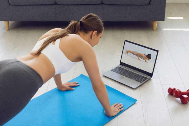 Fitness online. Young fit girl at home on the floor doing exercises, stretching warm-up and uses a video fitness lesson on the Internet. - Foto, Imagen