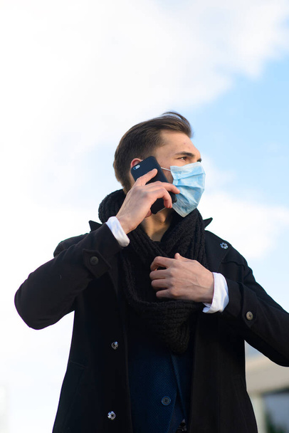 Portrét mladého pohledného obchodníka s obličejovou maskou v karanténě chřipky. Fotografie v kofeinu s laptopem, mobilní telefon. Koronavirová pandemie. - Fotografie, Obrázek