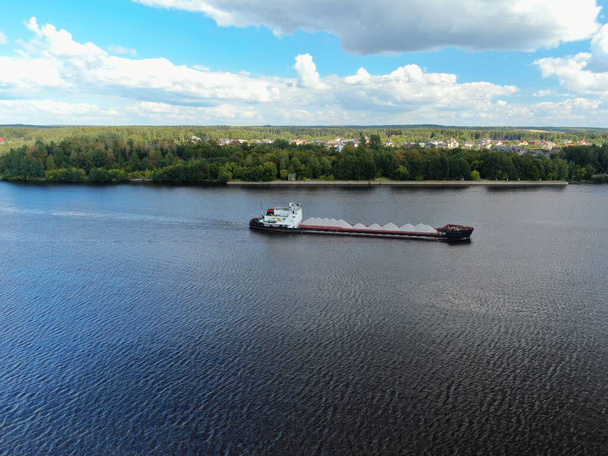 Aerial view cargo merchant ship sails along the river. Transport of goods by river barges. Beautiful landscape of the river. - Fotó, kép