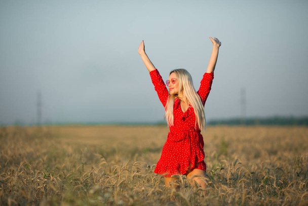 beautiful young woman in a red dress in a field in summer with hands raised up - Foto, afbeelding