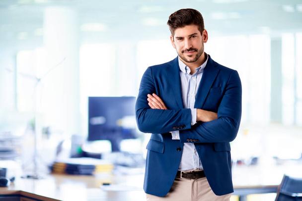 Retrato de hombre de negocios guapo con camisa y chaqueta mientras está de pie con los brazos cruzados en la oficina.  - Foto, imagen