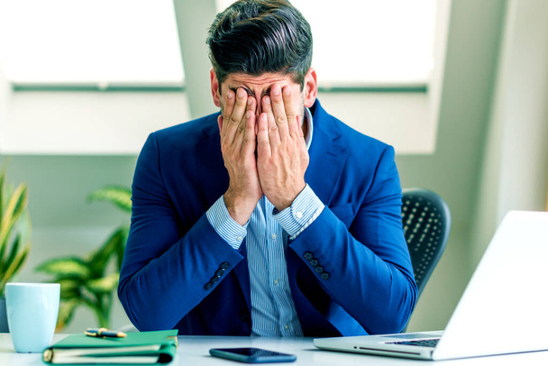 Shot of exhausted businessman with hands on his forehead sitting in the office. - Photo, Image