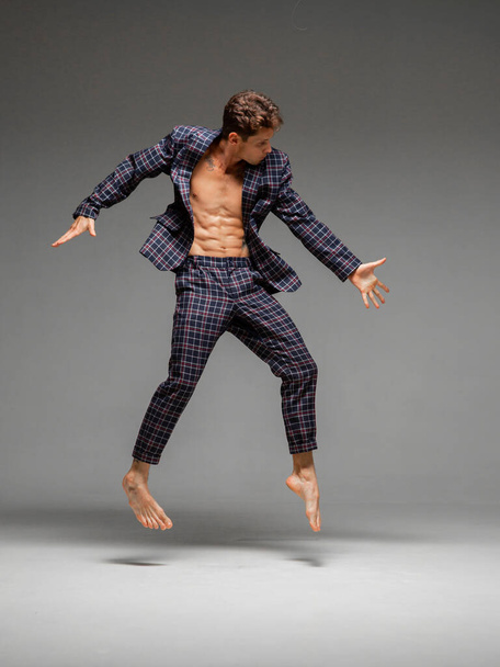 Stylish young guy dancer jump and levitate in studio isolated on gray background - 写真・画像