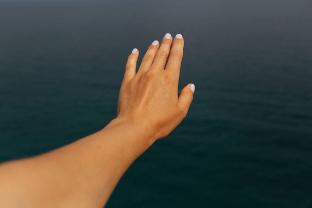 Summer vacation, beach relaxation, holiday. Female hand on blurred background of blue sea on summer day. Close-up. Selective focus. Copy space. - Fotoğraf, Görsel