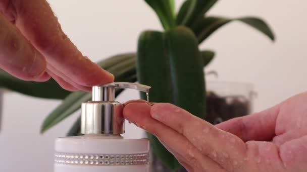 Dispensador de empuje masculino y jabón líquido exprimido a mano, primer plano disparado contra un fondo blanco y hojas - Metraje, vídeo