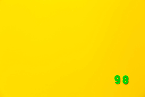 Um número de brinquedo de plástico verde noventa e oito está localizado no canto inferior direito em um fundo amarelo. - Foto, Imagem
