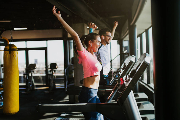 Young fit man and woman running on treadmill in modern fitness gym. - Photo, image