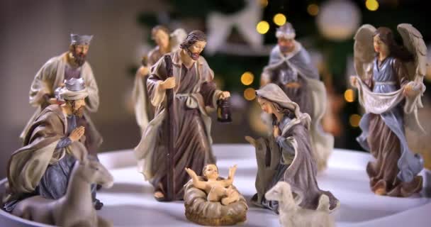 Natividad de Jesucristo con luces atmosféricas frente al árbol de Navidad sobre una mesa blanca. Escena de Navidad con figuritas. Dolly disparó 4k - Metraje, vídeo