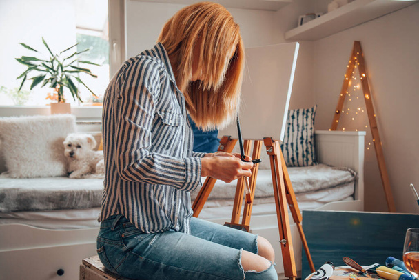 Beautiful artist woman painting in her room while texting on a cellphone. - Photo, image