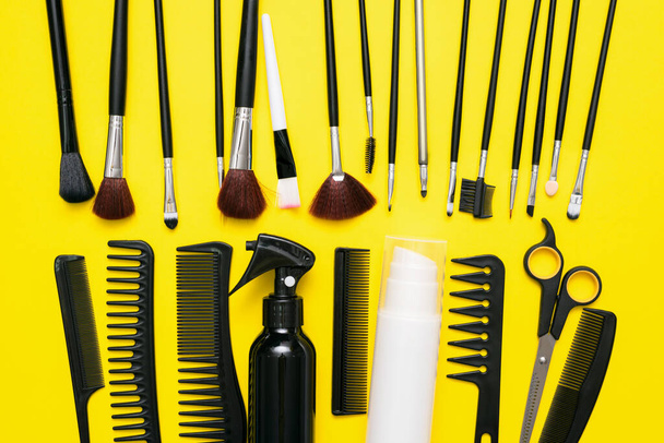 Makeup brushes, scissors and hairbrushes on the yellow flat lay background. - Foto, immagini