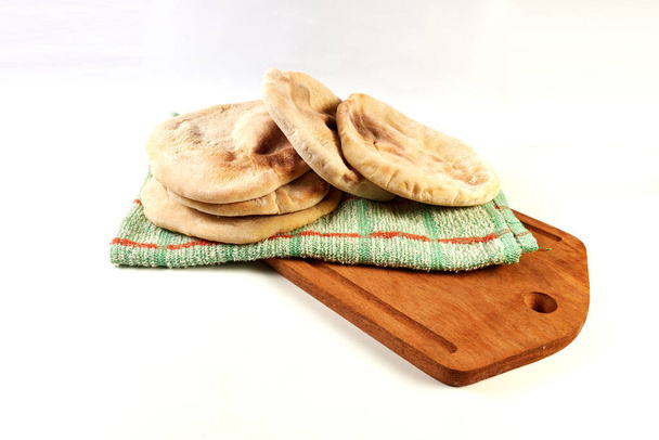pita recién horneada o panes árabes sobre un paño rústico y una tabla de madera sobre una superficie blanca - Foto, Imagen