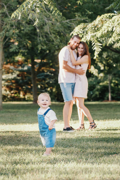 Happy smiling mother and father with baby boy in park outdoor. Family Caucasian mom and dad with son walking hugging in park on summer day. Happy family authentic lifestyle concept. - Foto, afbeelding