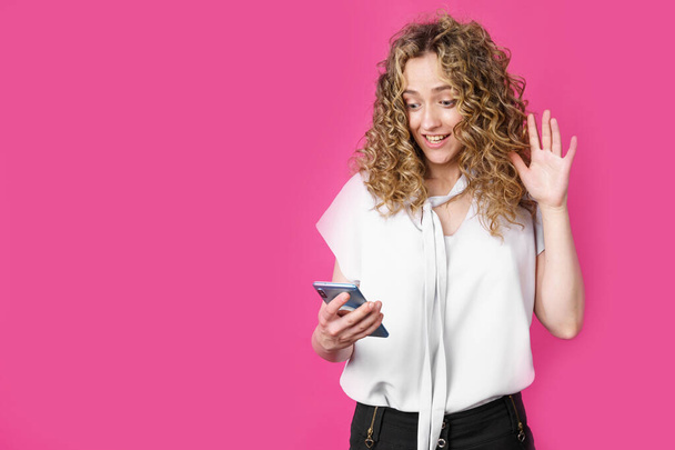 Young woman communicates through the phone by video link, expressing emotions. Female portrait. Isolated on pink background - Photo, image