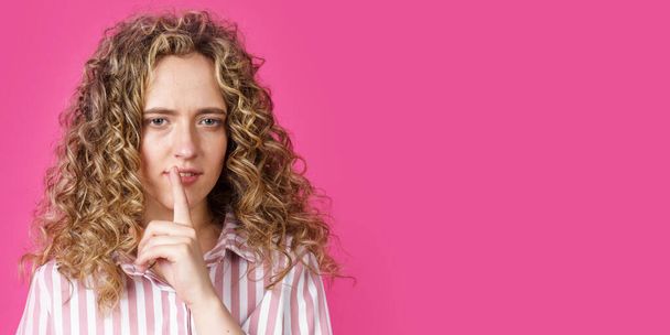 A young woman makes a gesture with her hands quietly, applying them to her lips. Isolated on pink background - Fotoğraf, Görsel