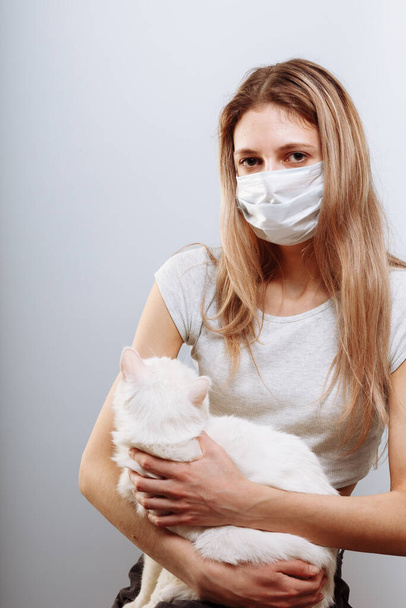 Frau in Schutzmaske hält Katzenhaustier in Gesichtsmaske. Chinesische Coronavirus-Krankheit COVID-19 ist gefährlich für Haustiere. - Foto, Bild