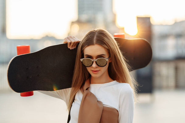 Portrait of a woman with a skate on his shoulder. Beautiful summer evening in the city. - Foto, imagen