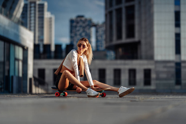 Bionda sexy con occhiali seduti su uno skateboard. - Foto, immagini
