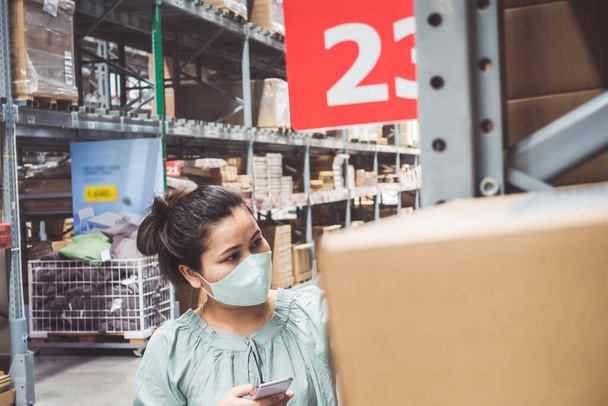 Asiatische Kundin trägt Gesichtsmaske mit Einkaufswagen im Supermarkt-Kaufhaus, während sie während der Covid-19-Pandemie Waren auswählt und im Regal sucht. Coronavirus-Covid-Situation  - Foto, Bild