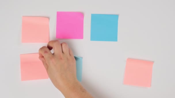 female hand gluing blank square multicolored stickers on white board, business concept - Footage, Video