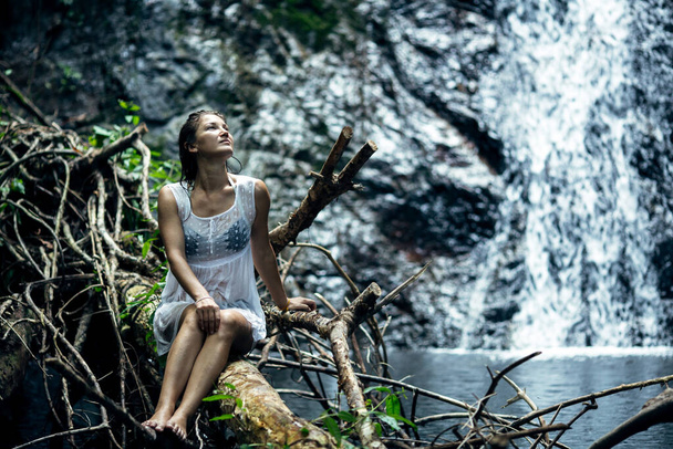 Schöne Frau sitzt in der Nähe eines Wasserfalls. Thailand. - Foto, Bild